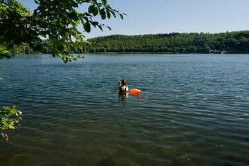 Woman open water swimming in a calm lake with an orange safety buoy © Turner