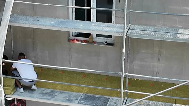 Construction worker installing insulation on building facade from scaffolding