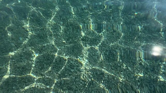 Oludeniz, T&uuml;rkiye. Clear water surface with sunlight reflections revealing pebbles and stones on the bottom, showcasing the underwater landscape in a serene aquatic environment