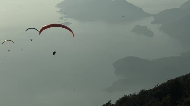 Fethiye, T&uuml;rkiye. Paragliders soaring over a serene landscape with mountains and islands visible in the distance, showcasing the beauty of aerial adventure in a tranquil setting