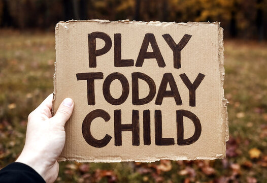 Hand holding a cardboard sign with play today child written in bold letters outdoors