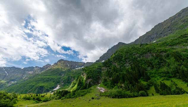 Lush alpine valley beneath rugged peaks and clouds