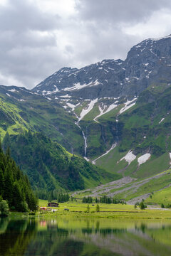 Dramatic close-up of majestic waterfalls plunging down the steep green cliffs and snow-covered slopes of the Felbertal valley near Hintersee, Hohe Tauern, Austria