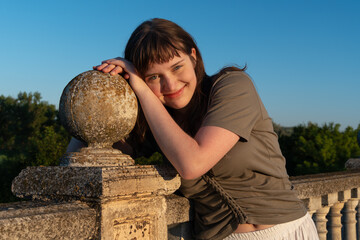 Naklejka premium Smiling young woman leaning on stone balustrade at sunset