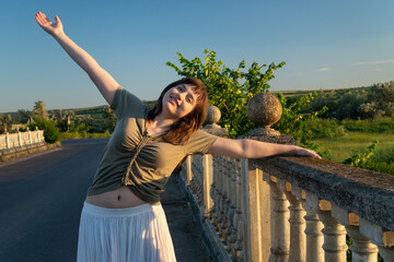 Naklejka premium Happy young woman enjoying freedom on a stone bridge at sunset