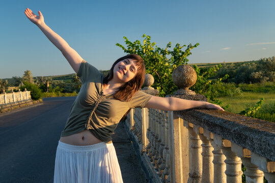 Happy young woman enjoying freedom on a stone bridge at sunset