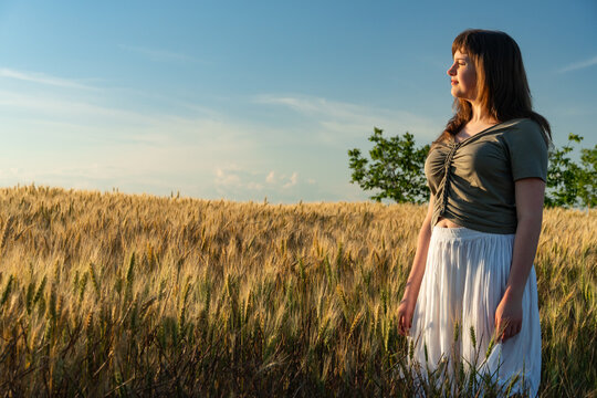 Young woman standing in a golden wheat field at sunset