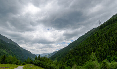 Fototapeta premium Winding road through a forested alpine valley under storm clouds