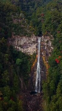 Spectacular aerial drone footage beginning at the iconic Nachi Falls (Nachi no Taki) and flying toward the historic Seiganto-ji Temple and the famous three-story Nachi Pagoda in Wakayama, Japan. Surro