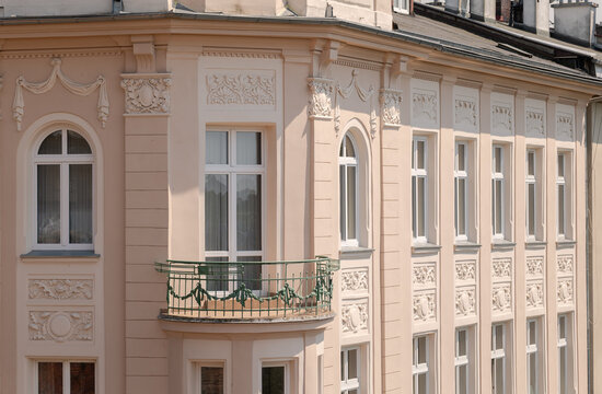 Elegant pale peach European tenement house facade with ornate stucco reliefs, arched white windows and curved iron balcony, sunlit historic residential architecture exterior, no people