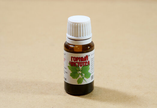 Small amber glass bottle of Mountain Celandine cosmetic liquid with Cyrillic label, white screw cap and botanical illustration on a brown background, front view with copy space