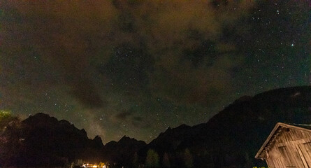 Mystical night sky with visible stars and drifting clouds over silhouetted alpine mountain peaks and a wooden hut, Dolomites, South Tyrol, Italy © Franziska Brueckmann