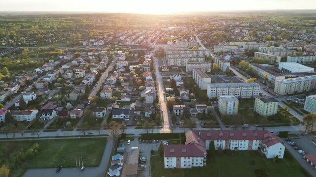 Aerial view of Konskie town, Poland, featuring the city park lake, surrounding green trees, parish cemetery, and urban landscape at sunset.