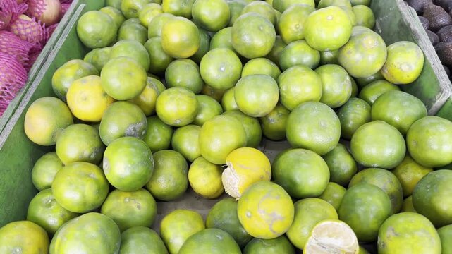Close up of fresh local green oranges stacked on display at traditional market