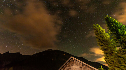 Mystical night sky with visible stars and drifting clouds over silhouetted alpine mountain peaks and a wooden hut, Dolomites, South Tyrol, Italy © Franziska Brueckmann