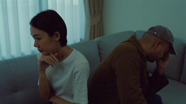 Sad Asian man and woman ignoring each other on the couch. Concept of emotional distance, family crisis, divorce, breakup and psychological stress.