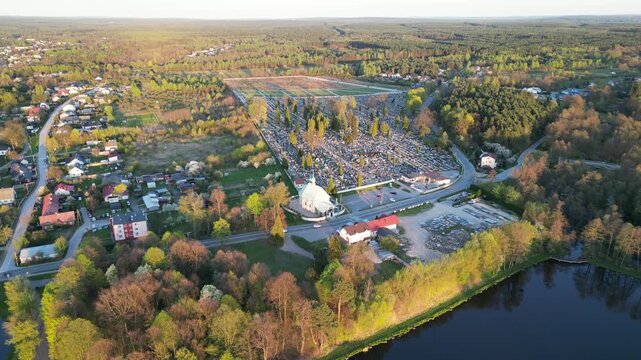 Aerial view of Konskie town, Poland, featuring the city park lake, surrounding green trees, parish cemetery, and urban landscape at sunset.