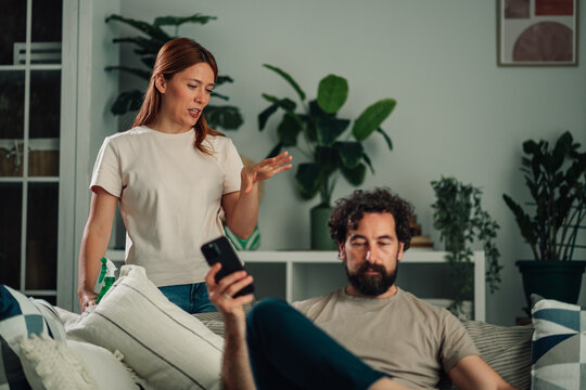 Woman arguing with man absorbed in smartphone, highlighting phubbing and relationship conflict over household responsibilities