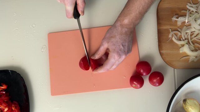 Overhead kitchen scene with hands slicing ripe tomatoes into thin pieces on coral cutting board during meal prep for fresh salad and simple home cooking, with tomato, slicing, knife, cuttingboard