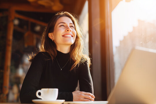 Young woman smiling at laptop in warm cafe light with coffee cup for online learning remote work creative focus lifestyle education productivity freelancer inspiration concept small business