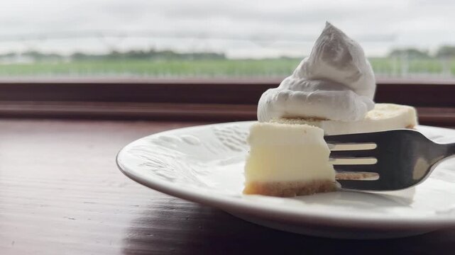 Whipped cream crowns cheesecake slice as fork slowly captures the first bite
