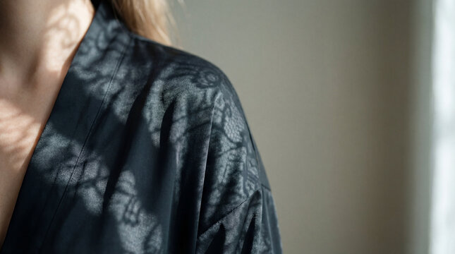 Close up of female shoulder neck in black satin robe with delicate lace shadow pattern across fabric skin creating elegant sensual fashion detail for luxury lingerie wellness editorial design concepts