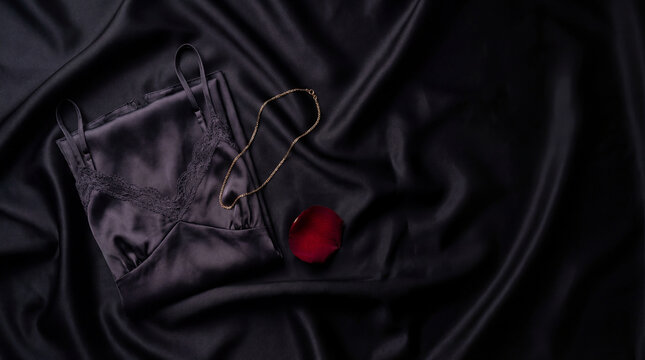 Black satin lingerie top with lace trim gold necklace red rose petal on dark silk fabric for elegant intimate fashion romantic gift luxury styling boudoir flat lay premium scene detail