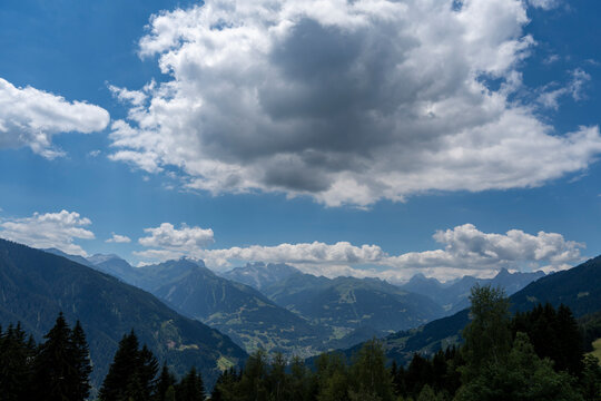 Scenic panoramic view from Kristberg mountain overlooking the lush green Montafon valley and the majestic Silvretta and R&auml;tikon mountain ranges under a dramatic cloudy blue sky in Vorarlberg, Austria