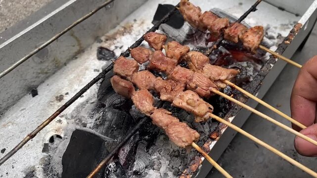 Sate Buntel (Culinary specialty from Solo, Central Java, Indonesia), featuring minced goat meat wrap in fat and grilled over charcoal with billowing smoke. Selective focus