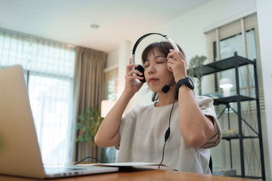 Asian Female student putting on a headset before attending an online class at home using a laptop computer.