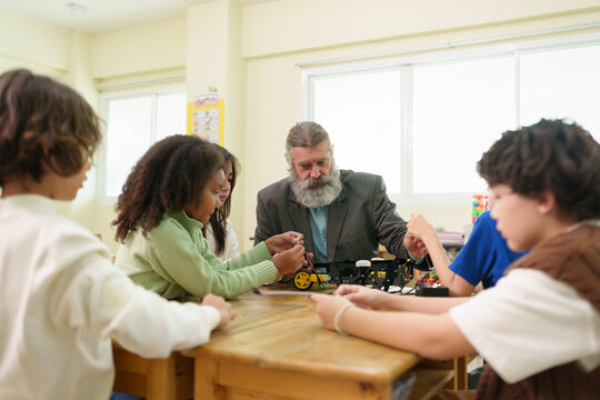 Male teacher guiding multiracial students during a robotics lesson focused on science, technology and engineering skills.