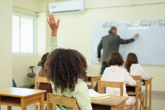 African schoolgirl raising her hand to answer or ask a question during a lesson in a multicultural classroom.