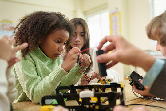 African girl concentrating on a robotics project during a STEM education lesson with multicultural classmates.