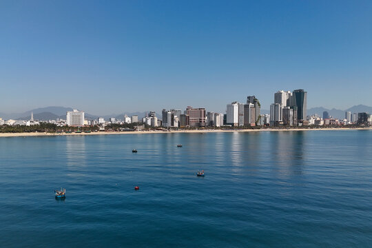 Coastal Da Nang city features many tall buildings next to My Khe Beach, where turquoise ocean water meets golden sand under a clear sky