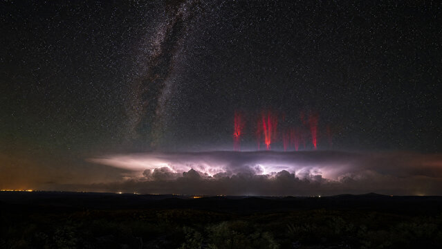 Red sprites flashing above a distant thunderstorm under the Milky Way at night