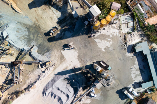 Aerial perspective shows a large concrete plant processing materials. Trucks load and unload near silos and aggregate piles during a sunny day