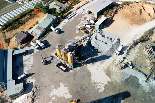 Overhead view of an active industrial site with yellow silos, conveyor belts, gravel piles, and heavy machinery, showing processing activity in sunlight