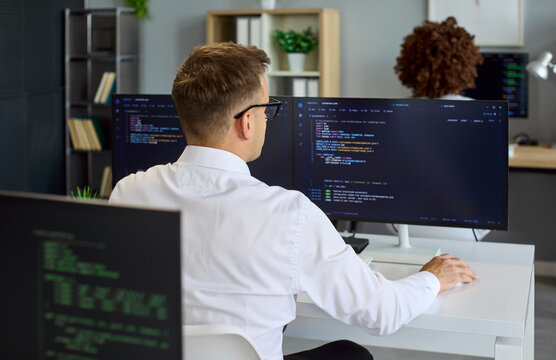 Programmer developer coding software monitors office computer. Engineer debugging on dual displays with concentration, refining code precisely. Clear concept of focused software development.