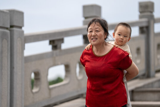Asian grandmother walking on stone bridge with toddler on her back