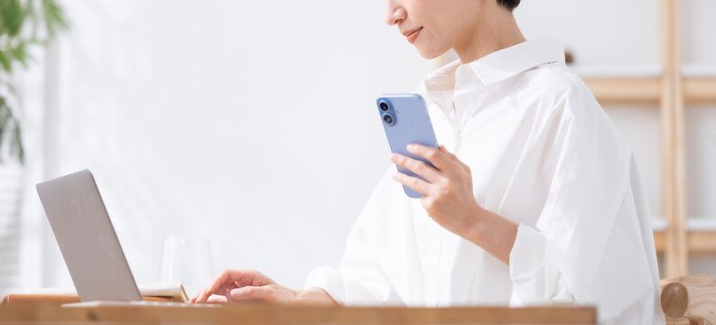 スマホを持ってパソコンを使う女性