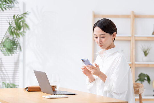 スマホを持ってパソコンを使う女性