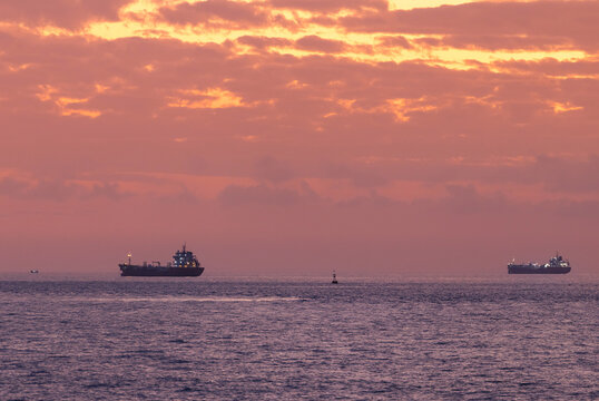 Oil tanker ships anchored near horizon under colorful dawn sky, concept waiting for Strait of Hormuz unblocking