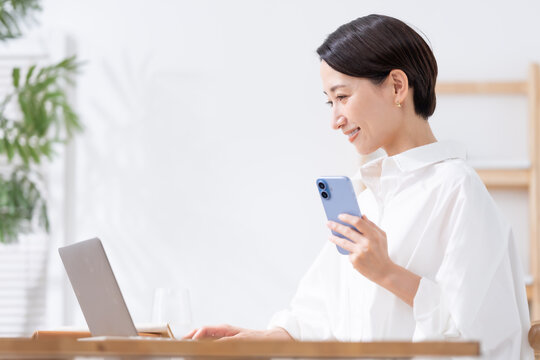 スマホを持ってパソコンを使う女性