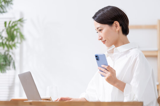 スマホを持ってパソコンを使う女性