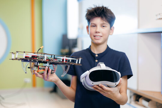 Happy child boy holding drone and virtual reality headset in classroom workshop