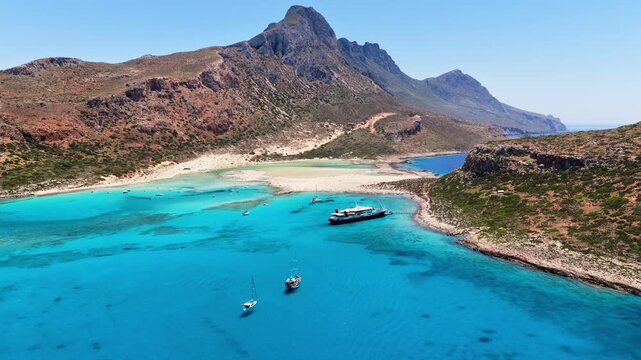 Aerial drone view of Balos Lagoon with its white-sand tombolo in vivid turquoise water below a rocky mountain, Balos, Greece