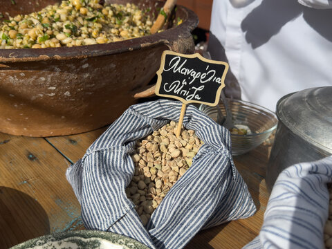 A striped fabric bag of raw manarolia or mpiza legumes with a Greek chalkboard sign, an ingredient for traditional fotokolyva salad on a rustic table.