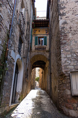 Fototapeta premium Vertical perspective of a narrow cobblestone street passing under a historic stone archway with traditional shuttered windows and balconies in the medieval hill town of Stroncone, Umbria, Italy