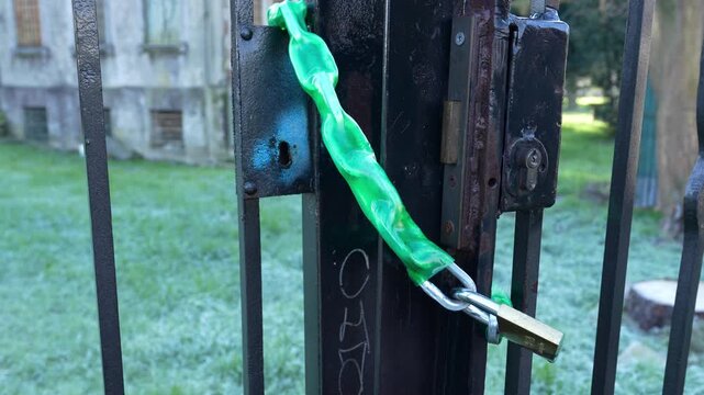 Green safety chain and padlock on an abandoned house gate symbolizing security and protection