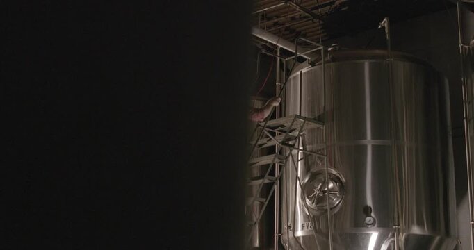 Brewmaster inspecting stainless steel brewing tank inside modern craft brewery production facility